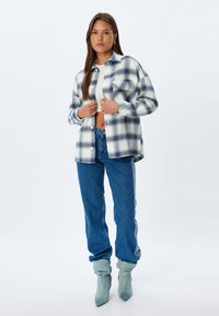 Camisa de cuadros de gran tamaño en azul y blanco, con bolsillos frontales, combinada con jeans de cintura alta en azul claro y botas de tela en azul claro hasta el tobillo.