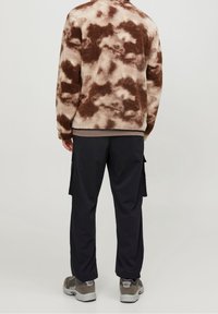 Fleecejacka med brunt och krämfärgat molnmönster, avslappnad passform, i kombination med marinblå cargobyxor och grå sneakers. Strukturerad och varm look.