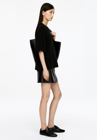 Schwarzer übergroßer Pullover aus weichem Material, kombiniert mit einem schwarzen Minirock aus Leder und schwarzen Sneakers, dazu eine große schwarze Tragetasche.