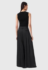 Sort ribbet tanktop kombineret med sorte bukser med brede ben og plisseringer. Fokus på enkel, struktureret design og glat stoftekstur.