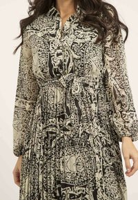Robe à motifs noir et crème avec un col, fermeture à boutons sur le devant, manches longues et taille ceinturée. Texture transparente avec des motifs complexes.