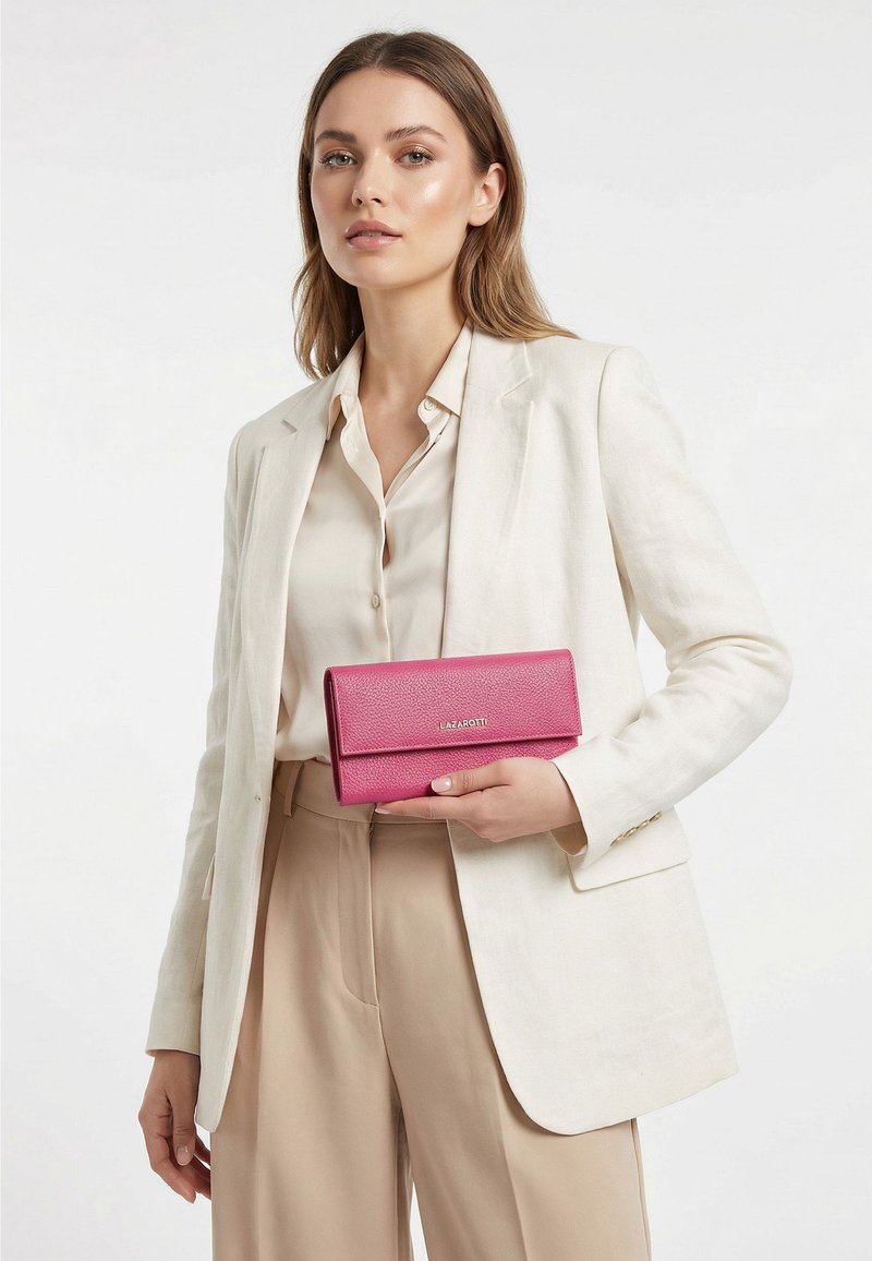 Mujer con traje beige sosteniendo una cartera de cuero rosa con el nombre de la marca Lazarotti visible en la solapa frontal.