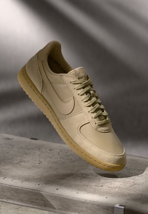 Beige Leder-Sneaker mit strukturierter Oberfläche, runder Spitze und flachen Schnürsenkeln. Mit einem Nike-Swoosh und einer Gummisohle mit genähter Optik.