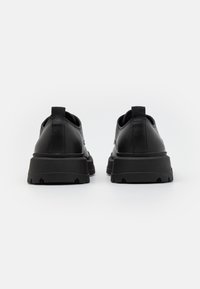 Scarpe in pelle nera con suola spessa e testurizzata, design arrotondato e linguette posteriori per un facile indossamento.