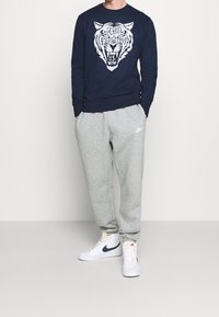 Sweat-shirt bleu marine avec un motif de tigre blanc, pantalon de survêtement gris et baskets montantes blanches avec une touche de bleu marine. Tenue décontractée et confortable.