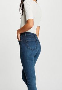 Niebieskie jeansy z wysokim stanem o slim fit, wykonane z denimu. Charakteryzują się tylnymi kieszeniami oraz dekoracyjnymi ćwiekami wzdłuż boku.