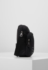 Borsa in tessuto nero con forma arrotondata, dotata di doppi scomparti con zip, tracolla removibile e logo discreto sul lato.