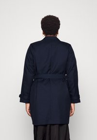 Cappotto trench navy con vita cintrata, ampio colletto e maniche con risvolto. Presenta un design su misura e un tessuto morbido e texture.