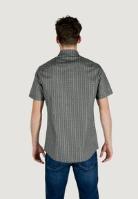 Camicia a maniche corte, tessuto a motivi bianco e nero, colletto standard, orlo curvo, indossata con jeans blu scuro. Cuciture e dettagli dei bottoni visibili.