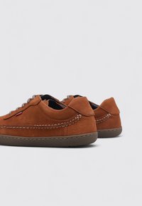 Baskets en daim marron à profil bas, avec des coutures, un bout arrondi et une semelle en caoutchouc texturée. Équipées d'un système de laçage et d'une marque discrète.