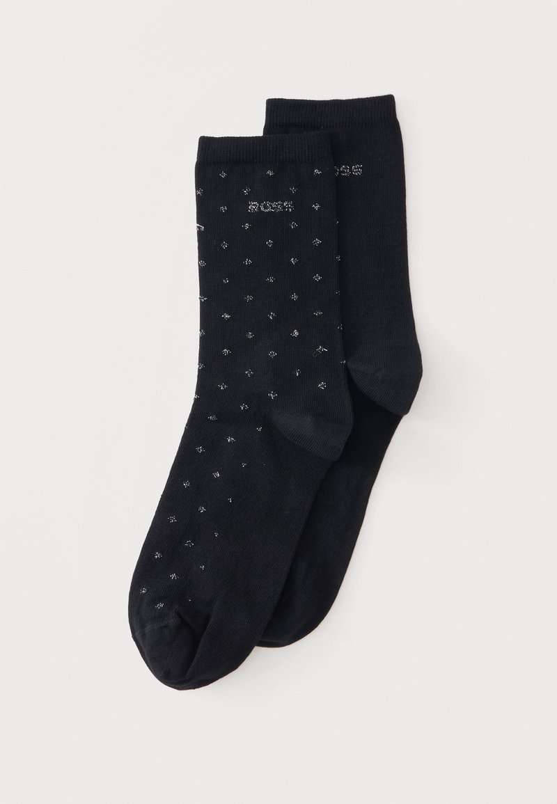 Paire de chaussettes noires de type crew, l'une avec un petit motif à pois blancs, l'autre unie, placées à plat sur un fond blanc.