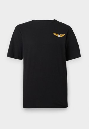 Μαύρο κοντομάνικο μπλουζάκι με ένα μικρό κίτρινο φτερωτό έμβλημα και ένα λευκό γεωμετρικό σχήμα στο πάνω αριστερό μέρος του στήθους.