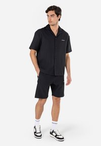 Chemise noire à manches courtes avec une texture côtelée subtile, assortie à un short. Présente un petit logo et des baskets blanches contrastantes.