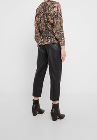 Blouse à manches longues imprimée avec un motif floral texturé dans des tons terre, associée à un pantalon en cuir noir raccourci et des bottines.