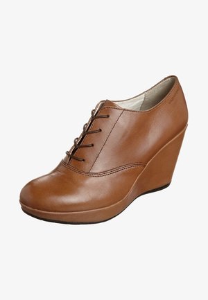 Chaussure à talon compensé en cuir marron avec fermeture à lacets à l'avant et bout rond lisse, présentée de côté pour montrer le profil extérieur et le bord de la semelle.
