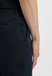 Die Navy-Hose verfügt über eine Gesäßtasche mit einem dezenten Logo, Reißverschlussdetails und einem glatten Stoff mit einer maßgeschneiderten Passform, die eine matte Textur präsentiert.