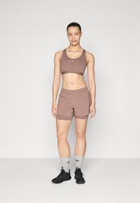 Soutien-gorge de sport marron et short assorti, avec un design ajusté, une taille élastique et des accents côtelés. Chaussures de sport noires et chaussettes grises.