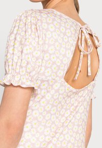 Blusa floral rosa con margaritas blancas y centros amarillos, mangas abullonadas y cierre atado en la parte posterior. Tejido suave y elegante borde con volantes.