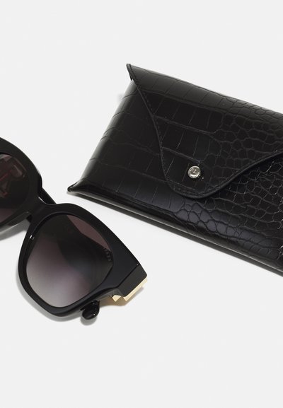 Black oversized sunglasses with dark gradient lenses, featuring a gold accent. Accompanied by a black faux-crocodile leather case.