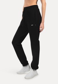 Schwarze Jogginghose aus weichem Material, mit einem Kordelzugbund, Seitentaschen und Slim Fit. Enthält ein kleines Logo-Detail.