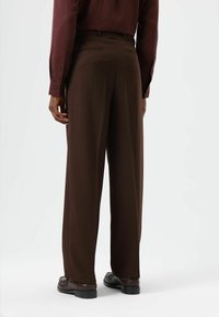 Bruine broek in een relaxte pasvorm, met een gladde textuur en rechte pijpen, gecombineerd met een donkerbordeauxrood shirt met lange mouwen en bruine schoenen.