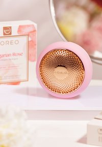 Cirkulär rengöringsanordning med ett rosa silikonutsidan och en glänsande roséguld texturerad yta. Vit förpackning i bakgrunden märkt "Ungersk Ros."