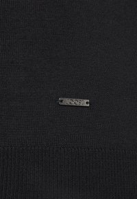 Tessuto a maglia nero con un'etichetta in metallo argento impresso con "JOOP!" sul lato, che mette in mostra una superficie liscia e un design raffinato.