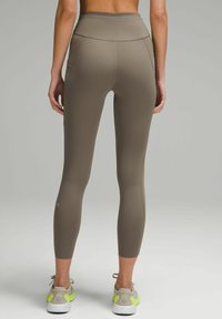 Legginsy o wysokim stanie w oliwkowym kolorze, wykonane z gładkiego, elastycznego materiału z płaskimi szwami i dopasowanym krojem, z bocznymi kieszeniami.