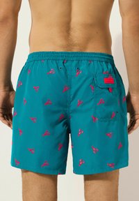 Shorts de bain teal en tissu léger, présentant un motif de homards rouges répétitif, une taille élastique et une poche arrière avec matériel.