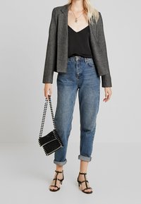 Grau strukturiertes Blazer über einem schwarzen Camisole, kombiniert mit hoch taillierten blauen Jeans. Eine schwarze Perlen-Handtasche und schwarze Riemchen-Heels vervollständigen den Look.