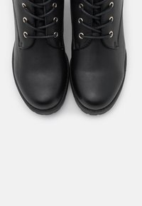 Bottes basses en cuir noir avec bouts ronds, dotées d'œillets métalliques, de lacets noirs et d'une semelle en caoutchouc texturée.