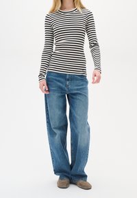 Maglia a maniche lunghe a righe bianche e nere abbinata a jeans blu larghi. La maglia ha una texture a coste; i jeans presentano il classico design a cinque tasche.