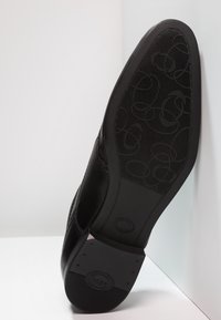 Chaussure en cuir noir avec une semelle en caoutchouc texturée. La semelle présente un design à motifs. Les bords sont lisses avec un minimum de détails.