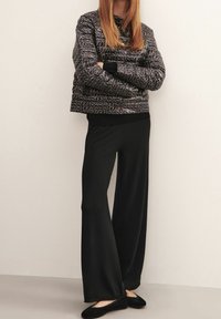 Quilted schwarze Jacke mit geometrischem Muster, kombiniert mit schwarzen Hose in weit geschnittener Form. Beide Kleidungsstücke haben eine glatte Textur und einen entspannten Schnitt.