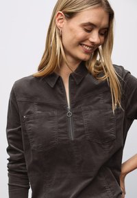 Houtskoolgrijze pullover met een halve ritssluiting aan de voorkant, twee borstzakken en een kraag. Zacht, gestructureerd stof met een ontspannen pasvorm en stikseldetails.