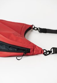 Rote wasserabweisende Slouch-Tasche mit einem schwarzen Reißverschluss, verstellbarem Tragegurt und Hakenverschluss. Verfügt über eine glatte Außenfläche und ein elegantes Design.