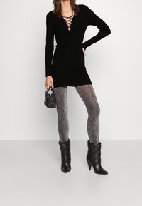 Svart stickad klänning med djup V-ringning och snörningsdetalj, i kombination med glittrande svarta leggings och svarta klackade ankelstövlar. Liten svart handväska.