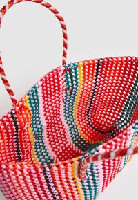 Tkany kosz z żywymi wzorami w kolorze czerwonym, różowym, zielonym i żółtym. Okrągły kształt z dwoma skręconymi uchwytami, wykonany z trwałego materiału syntetycznego.