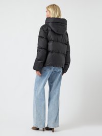 Chaqueta de plumas negra con capucha, con secciones acolchadas y una textura suave. Combinada con jeans de pernera ancha de color azul claro y tacones marrones.