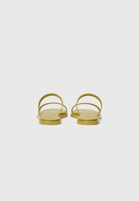 Gule flade sandaler med to buede stropper og en glat sål, der har et minimalistisk design og en mat finish.