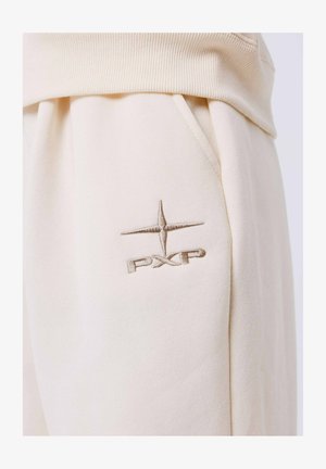 Pantalons de jogging beige en tissu doux, avec une taille côtelée et des poches latérales. Un logo "PXP" brodé est visible sur la poche droite.