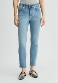 Jeans de denim azul claro con un diseño ajustado, estilo de cinco bolsillos y pequeños detalles de hardware metálico. Combinados con bailarinas decoradas en negro y plata.