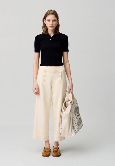 Haut noir à manches courtes à côtes, pantalon large crème avec des accents de bouton et mocassins marron. Tenant un sac fourre-tout en toile à motifs.