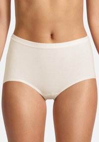 Kvinde iført højtsiddende beige bomuldsunderbukser, vist fra midt torso til midt lår mod en ensfarvet baggrund.