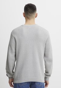 Pulover gri texturat cu un model în diamant, cu mansete și tiv striate, gât rotund, purtat peste blugi albaștri, văzut din spate.