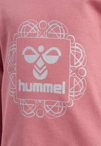Rosa Sweatshirt mit einem zentralen weißen Logo in einem dekorativen Rahmen, das den Markennamen "hummel" in einer modernen Schriftart zeigt.