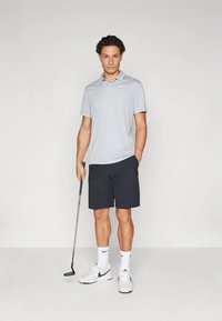 Polo de golfe cinza claro com mangas curtas, combinado com calções escuros. Meias brancas e ténis. Segurando um taco de golfe. Design simples.