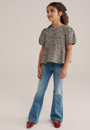 Leopardenmuster, kurzärmelige Bluse mit Puffärmeln, kombiniert mit ausgestellten blauen Jeans und roten Ballerinas. Glattes Material, lockere Passform.