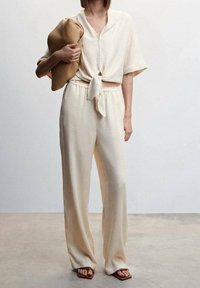 Ensemble décontracté de couleur crème comprenant un chemisier à manches courtes noué et un pantalon à jambes larges, fabriqué dans un tissu doux et texturé.