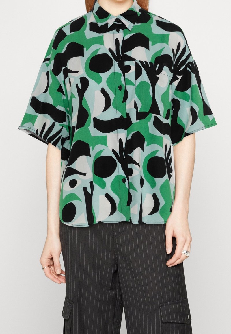 Chemise à manches courtes en vert, noir et gris avec des motifs abstraits. Caractérisée par un devant à boutons et une poche poitrine. Matière légère.